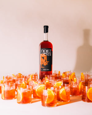 Large bottle of Negroni cocktail behind multiple glasses of cocktail