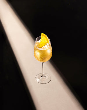 Pear & White Tea Fizz Cocktail in a clear wine glass with cubed ice garnished with a lemon slice.
