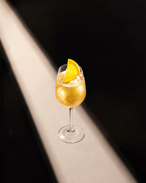 Pear & White Tea Fizz Cocktail in a clear wine glass with cubed ice garnished with a lemon slice.